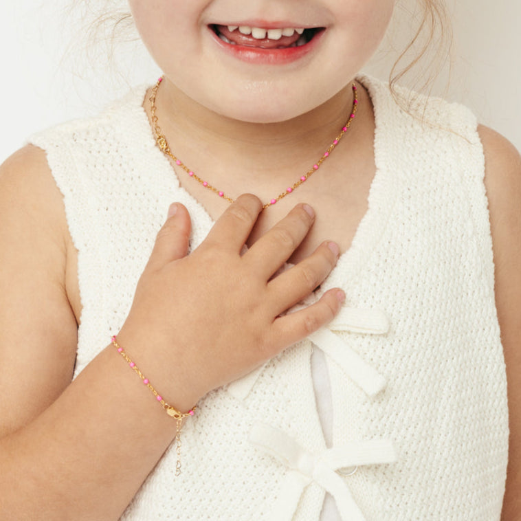 Child wearing a pink beaded necklace with a white background